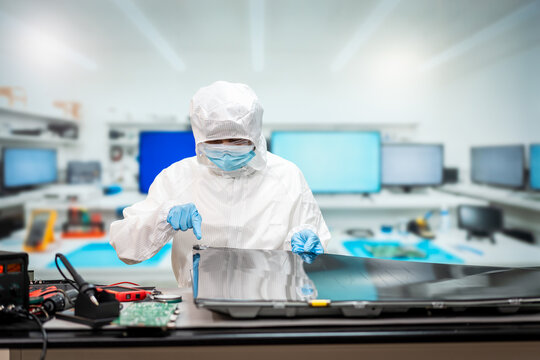 Forensic technician in protective coveralls and mask examines a laptop in a modern digital crime laboratory.