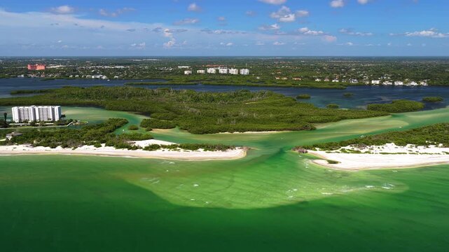 An aerial view shows a shallow green inlet opening to the sea between sandy beaches, with mangrove-covered islands, a sheltered waterway and buildings farther inland.