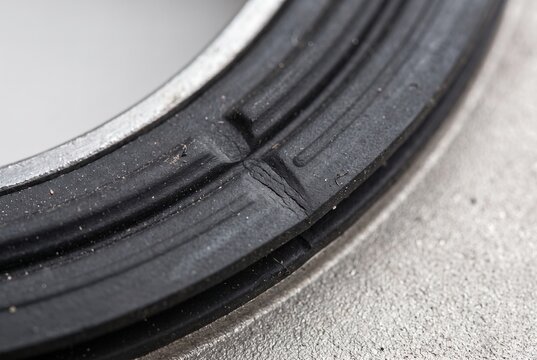 Cracked black rubber gasket ring on metal surface. Close up of damaged mechanical seal showing wear, aging, and material failure