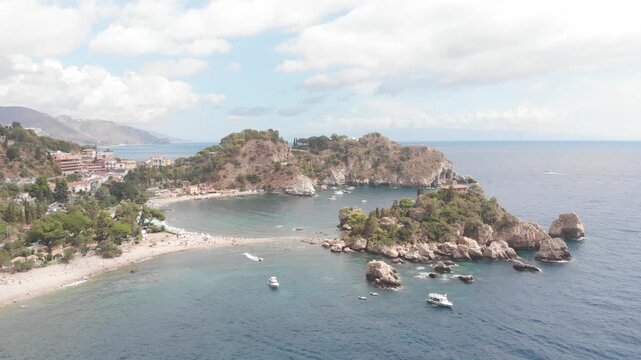 Aerial drone forward-moving shot flying toward Isola Bella off the coast of Taormina, Sicily, with the Mediterranean Sea surrounding the island.
