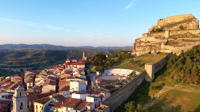 Warm sunset light over Morella in Castellon, Spain, with its hilltop castle ruins, ancient stone walls, red tiled rooftops, bullring and rolling mountains in the distance