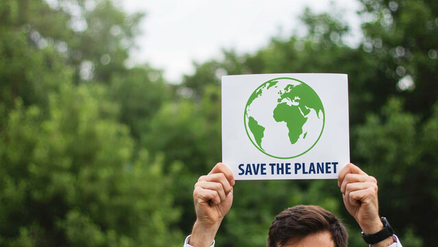 Person holding a sign with the Earth symbol and save the planet text during daytime against blurred green trees