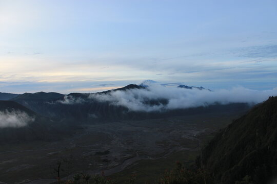 Scenic landscape of Mount Bromo caldera during early morning twilight with soft fog and volcanic steam floating over the mountain range in East Java, Indonesia.