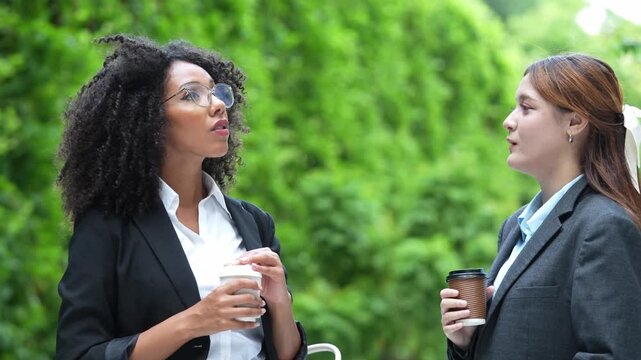 Diversity female employee walking with coffee cup and talking together at office building outdoors during a break