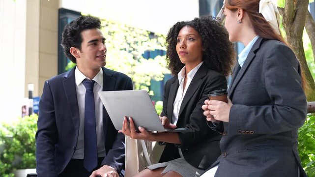 A diverse business team gathers outdoors to review project data on a laptop, collaborating efficiently and sharing ideas in a modern corporate setting.