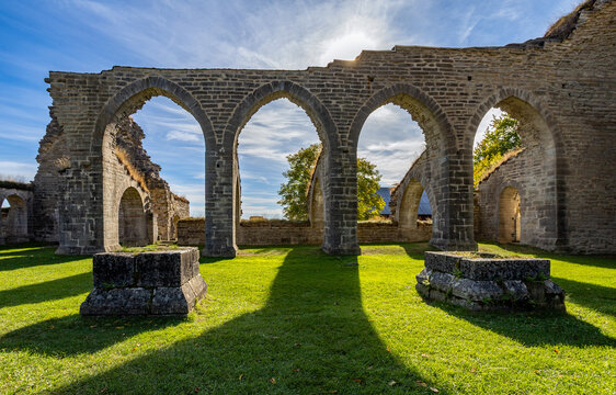 Pointed arches cast long shadows across the grass at the medieval Alvastra Abbey ruins in Sweden.