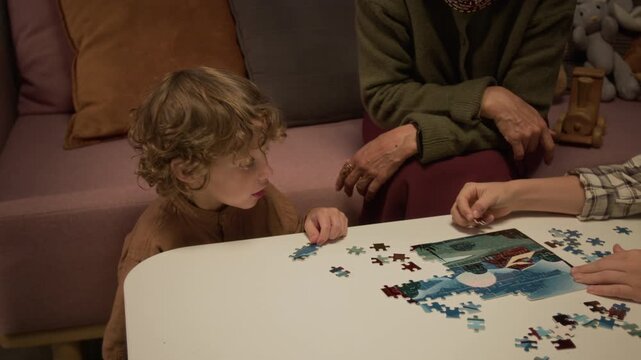 Caucasian senior woman helping young boys assembling jigsaw puzzle on table. Footage suitable for family bonding campaigns, early education projects, and senior leisure marketing