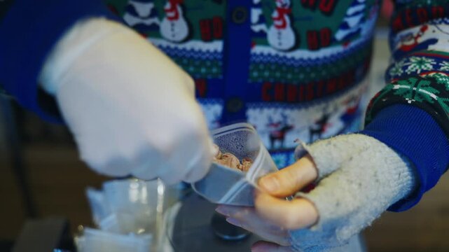 A person is holding a bag of candy peanuts packaging at Christmas market in Cologne, Germany. The person is wearing gloves and is standing in front of a scale