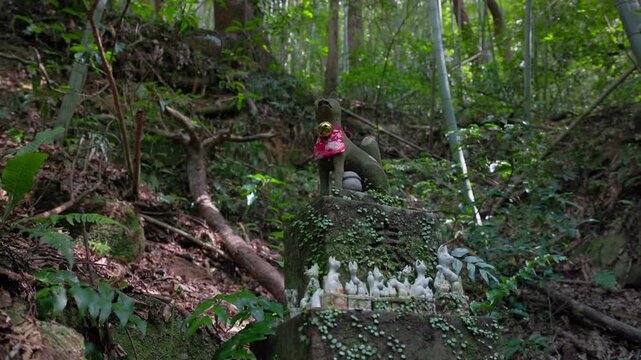 石の台座に並ぶ狐の置物とお地蔵さん 森の斜面