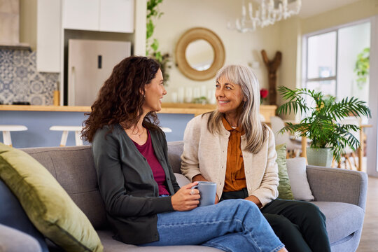 Happy senior woman with adult daughter taking a cup of tea at home