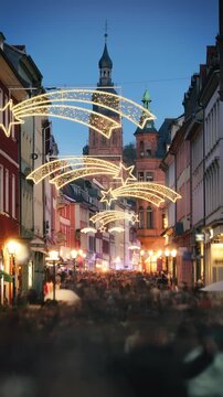 Loads of people with motion blur rushing and shopping on the historic German city of Heidelberg at Christmas. With holiday decoration and buildings leading to a church.