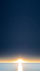 Fototapeta premium Sunrise or sunset over a calm sea under a starry night sky with bright sunburst and reflection on the water. Nature, natural or quotes background