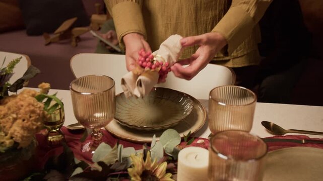 Caucasian woman setting festive dining table with ceramic plates and autumn decorations. Footage useful for Thanksgiving dinner campaigns, catering services, and holiday event promotions