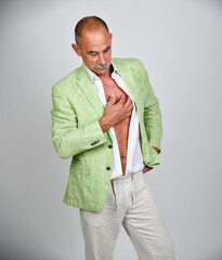 Naklejka premium Selbstbewusster älterer Mann im hellgrünen Sakko mit offenem weißen Hemd und Hand auf der Brust. Best Ager, Fashion, sommerliche Eleganz, Persönlichkeit, Lifestyle und moderne Studiofotografie.