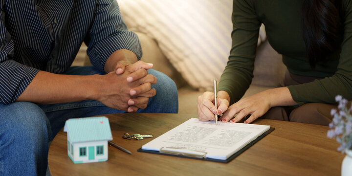 Homebuyer signing real estate contract beside house model and keys