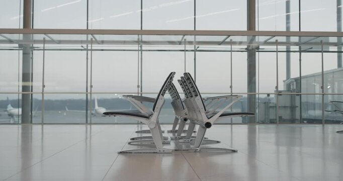 A row of empty lined chairs in front of a window at airport, establishing shot