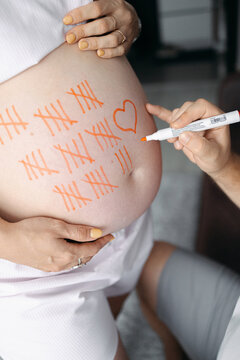 Pregnant woman with tally marks drawn on her belly, pregnancy countdown concept, expecting mother, birth anticipation, maternity lifestyle.