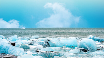 Stunning glacial icebergs resting on the dark volcanic sand of Diamond Beach in Iceland, with the cold sea and cloudy blue sky in the background during daylight. Climate change concept © Leo Lintang
