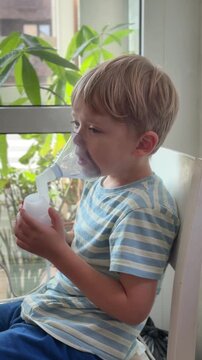 A young boy sits using a nebulizer mask for breathing treatment at home. Pediatric respiratory care, asthma, illness, recovery, medical treatment, health, family care.