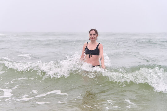Young woman standing in sea surf beneath pale foggy sky