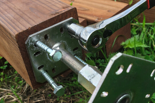 Installation of a galvanized steel base plate for a pergola on a treated wooden post, using lag screws.