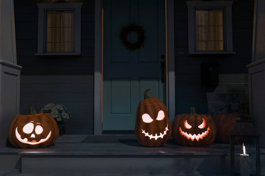 Spooky glowing jack-o'-lanterns welcome guests. Three illuminated carved pumpkins with distinct diverse faces adorn a dark suburban porch by a blue door. Happy Halloween card