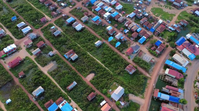 Aerial view of a floating village near Siem Reap, Cambodia, showing scattered homes, narrow waterways, dirt roads and green plots across a low-lying rural settlement.