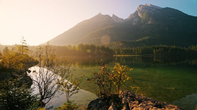 Painterly lake scenery in Germany with majestic mountains, trees, blue sky and clear reflections in the calm water at sunrise