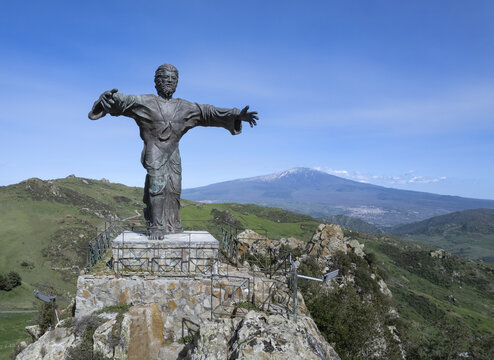 Aerial view of the bronze statue of Cristo Il Signore della Montagna standing on a rocky peak with Mount Etna in the background, in Cesaro, Sicily, Italy.