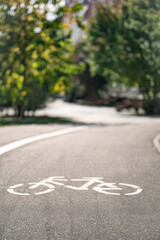 Obraz premium White bicycle road marking on an empty urban bike lane surrounded by green trees, sustainable mobility and cycling infrastructure with copy space. Vertical format.