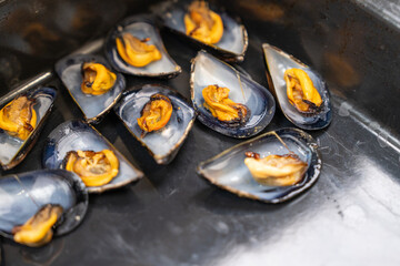Cooked mussel with orange meat in an open blue black shell, one of many steaming in a dark metal pan, a concept of gourmet cuisine and healthy eating. © Masarik