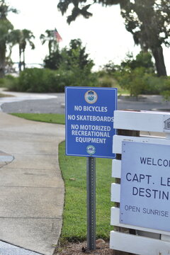 Blue park rule sign stating no bicycles, no skateboards, and no motorized recreational equipment at a public park entrance