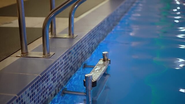 Luxury hotel spa pool with a blue tile wall and a metal railing forming a colofrul waves and ripples on illuminated water surface, slow motion