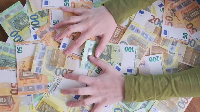 greedy hands grab euro banknotes across table symbolizing intense avarice and sudden wealth dream, person eagerly raking paper currency after winning fortune during jackpot lottery prize moment