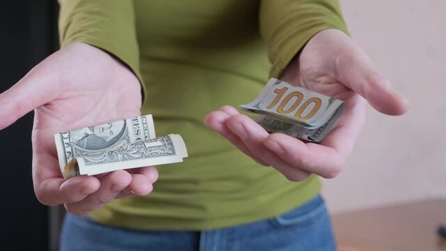 Person offers choice between closed hands showing one dollar bill and hundred dollar note indoors, symbolizing poor financial decisions, mistaken alternatives and regretful money gambles