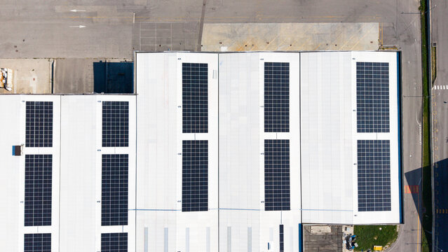 Aerial view of a logistics warehouse featuring rows of rooftop solar panels on a white industrial roof in Liscate, Lombardy, Italy.