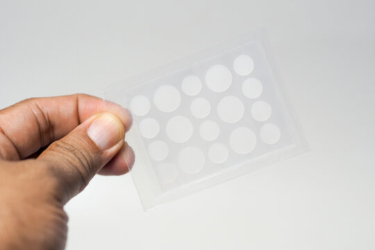 A hand holding a transparent sheet of round hydrocolloid acne patches in various sizes