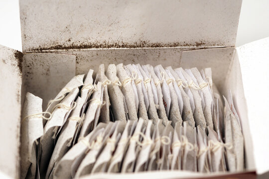 An open cardboard box filled with neatly arranged tea bags with strings attached