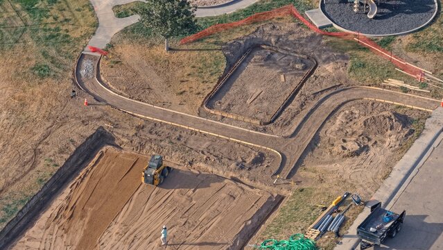 Aerial view of a construction site featuring a skid steer loader, excavated ground, and curved walkways in a park area in Eaton, Colorado, United States.