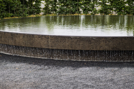 Water gently cascades over the edge of a circular stone fountain basin into a gravel surface.