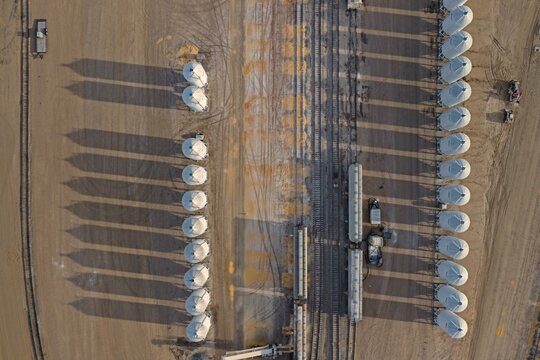 Aerial view of grain elevators arranged in parallel rows with long shadows cast across the industrial site near railroad tracks in Eaton, Colorado, United States.