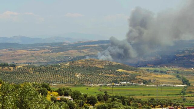 Large Smoke Plume Rising From Burning Hillside Above Valley 