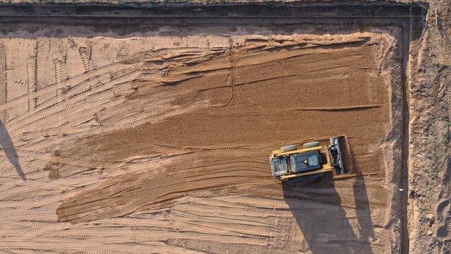 Aerial view of a yellow skid steer loader grading soil on a construction site with visible tire tracks in the dirt in Eaton, Colorado, United States.