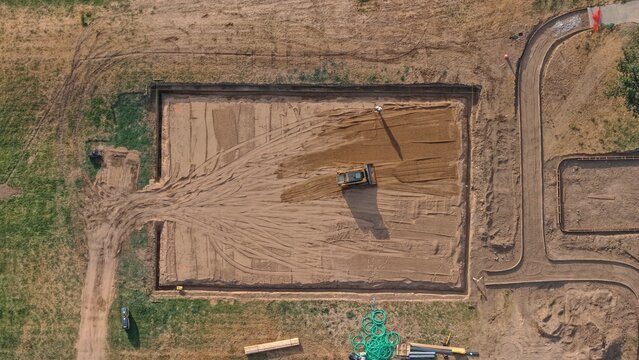 Aerial view of a bulldozer leveling a rectangular construction site with dirt tracks and surrounding green fields in Eaton, Colorado, United States.
