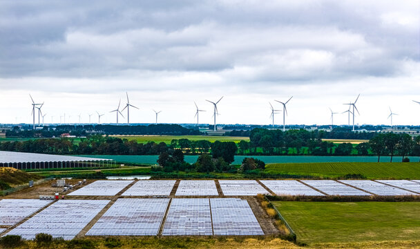 Aerial view of Agriport A7 solar farm with rows of photovoltaic panels in a rural landscape with wind turbines in the background in Middenmeer, Noord-Holland, Netherlands.
