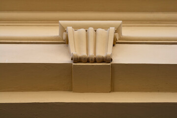 A straight on close up of a beige building exterior featuring a classic decorative stone corbel beneath horizontal moldings. © nahhan