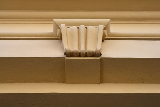 A straight on close up of a beige building exterior featuring a classic decorative stone corbel beneath horizontal moldings.