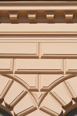 A vertical close-up view of a beige historic building facade featuring geometric block rustication patterns and horizontal decorative cornices. © nahhan