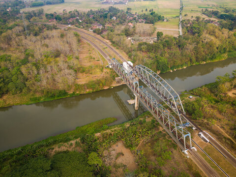 Aerial view of a steel truss railway bridge spanning a river, surrounded by lush tropical vegetation and rural landscape in Yogyakarta, Special Region of Yogyakarta, Indonesia.