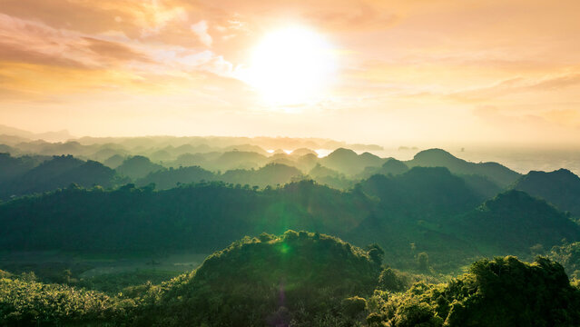 Aerial view of the lush green hills of Pantai Goa Cina during a golden sunset in Sumbermanjing Wetan, East Java, Indonesia.